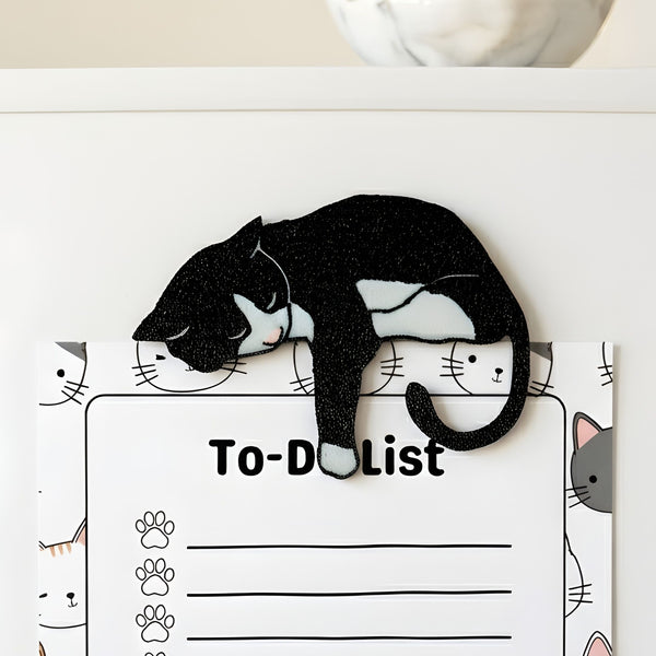 Black tuxedo cat fridge magnet holding a cat-themed to-do list on a refrigerator