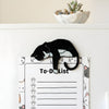 Black tuxedo cat fridge magnet holding a cat-themed to-do list on a refrigerator