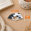 A small cat-shaped reading ring accessory with a white base and dark gray spots, shown on a wooden surface with measurement callouts indicating 3.6 inches in length and 1.
