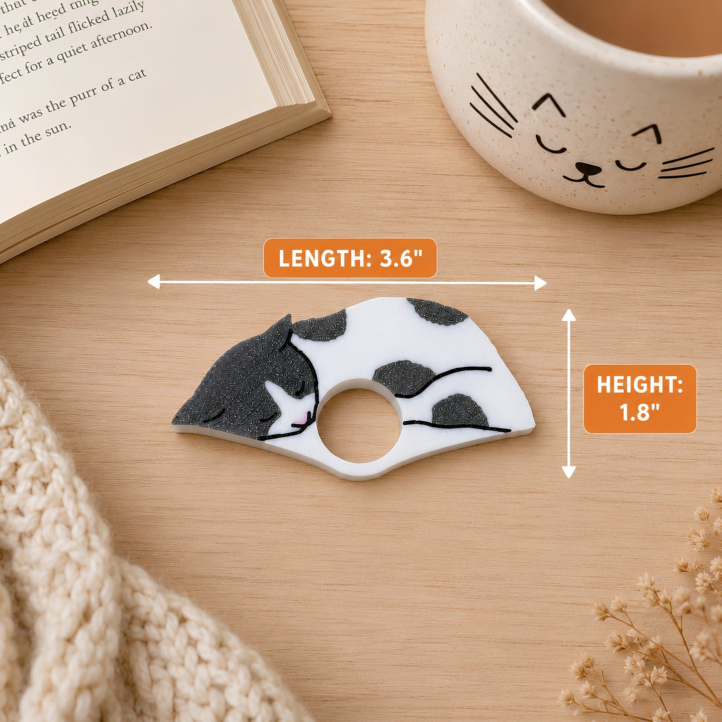 A small cat-shaped reading ring accessory with a white base and dark gray spots, shown on a wooden surface with measurement callouts indicating 3.6 inches in length and 1.