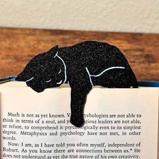 Black cat bookmark shown in a book holding onto a page with its paw dangling