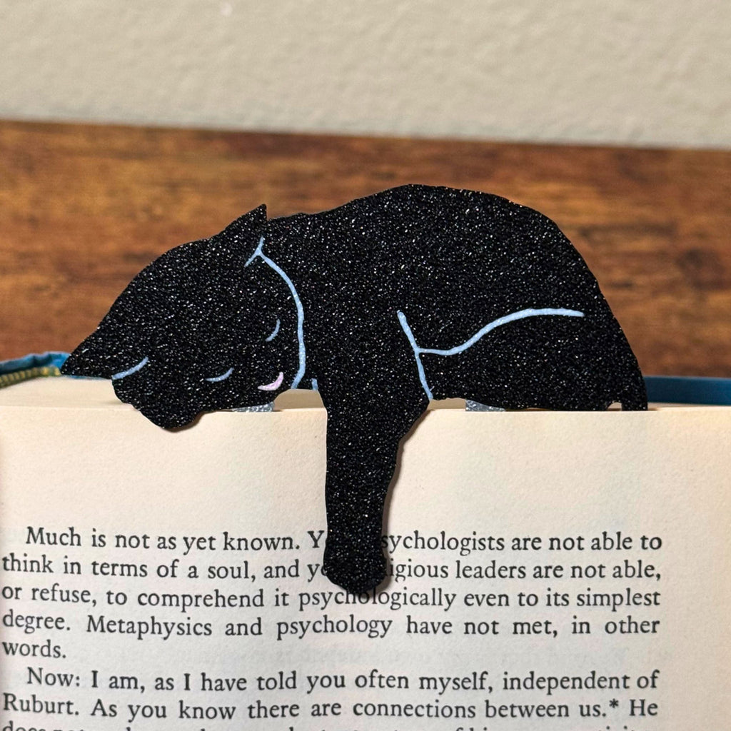 Black cat bookmark shown in a book holding onto a page with its paw dangling