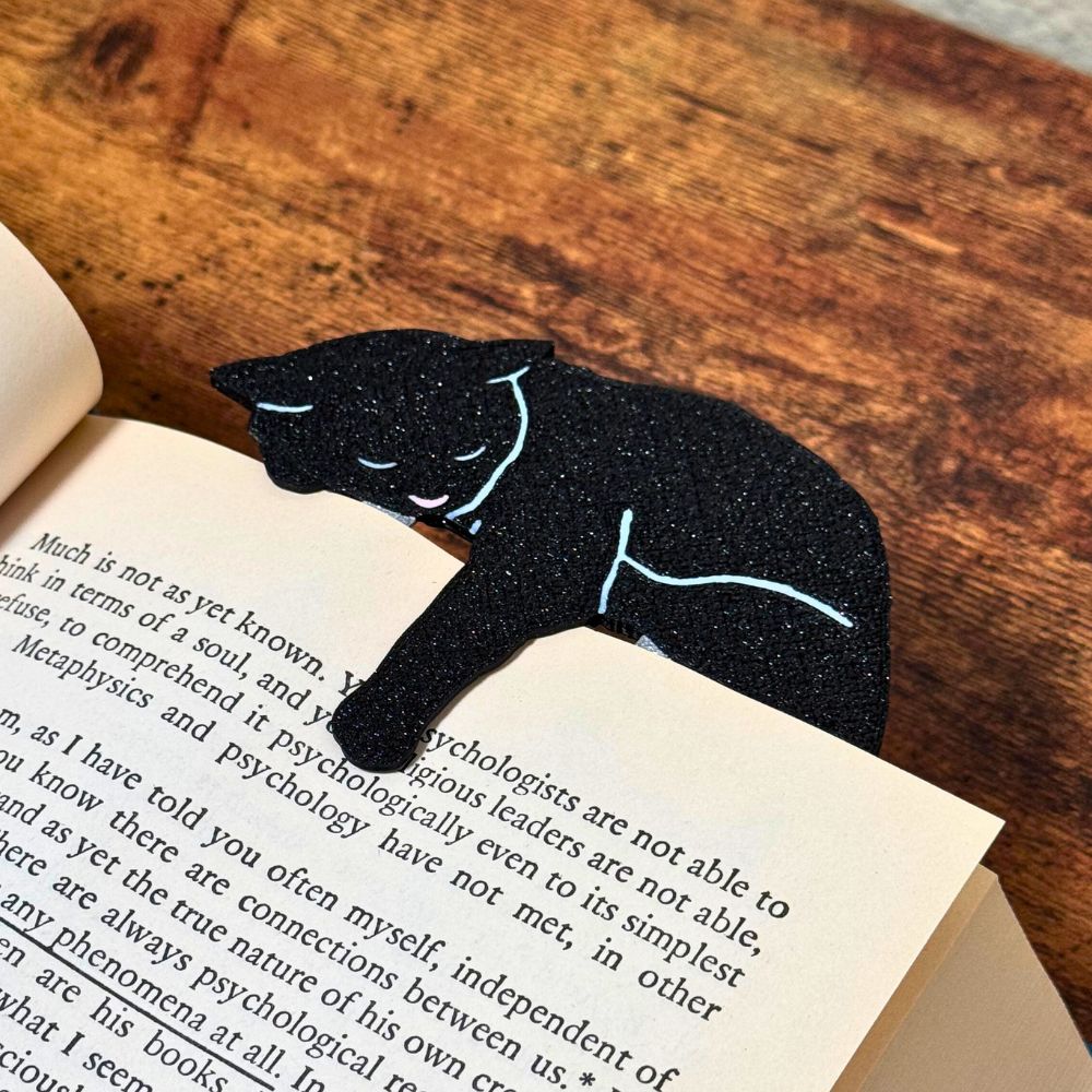 Black cat bookmark shown in a book from an angle holding onto a page with its paw dangling