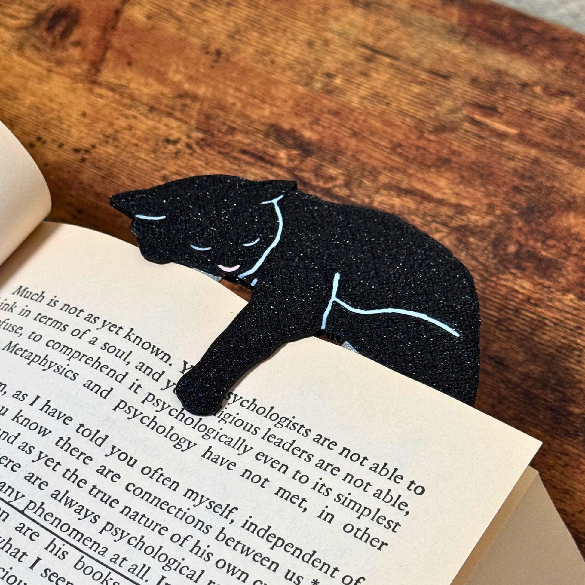 Black cat bookmark shown in a book from an angle holding onto a page with its paw dangling