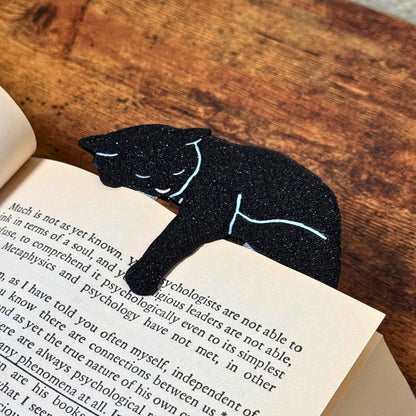 Black cat bookmark shown in a book from an angle holding onto a page with its paw dangling