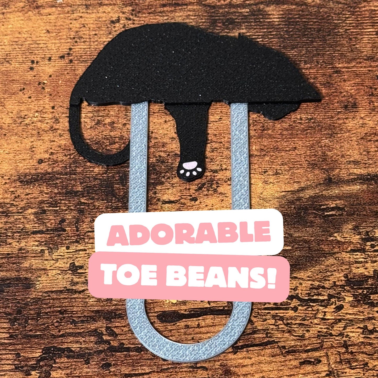 The back of a tuxedo cat bookmark showing the adorable pink toe beans on the back of its paw