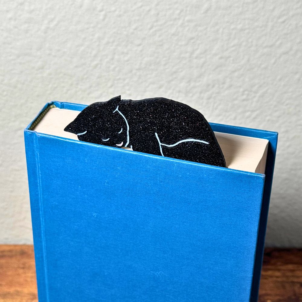 Black cat bookmark shown in a closed book taking a nap on top