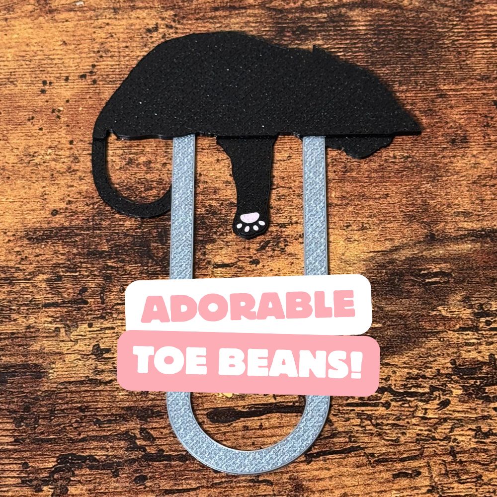 The back of a tuxedo cat bookmark showing the adorable pink toe beans on the back of its paw
