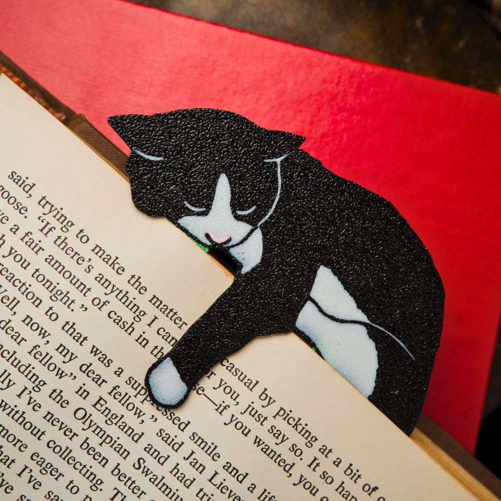Tuxedo cat bookmark shown in a book with a striking red background holding onto a page with its paw dangling