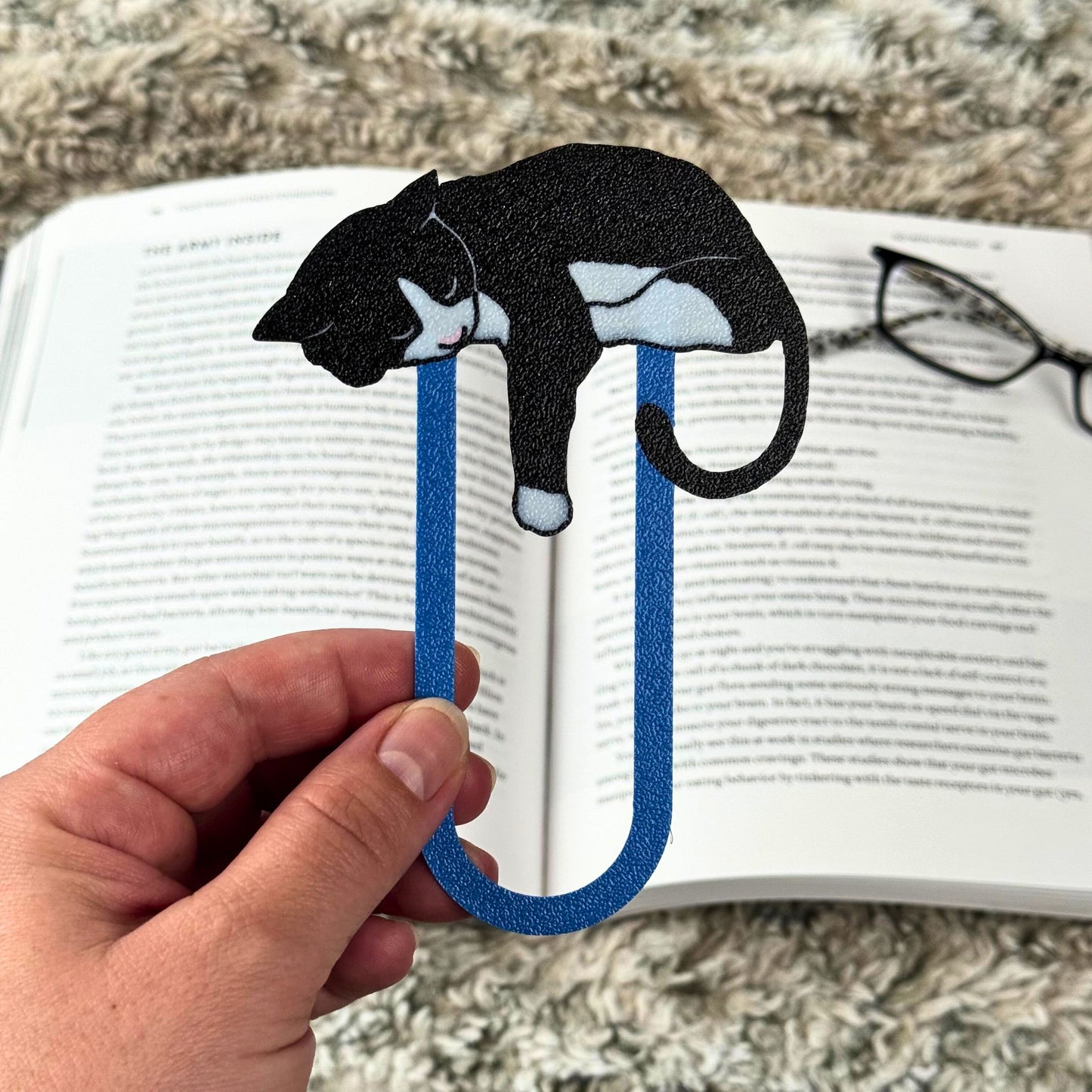 Tuxedo cat bookmark with a blue clip held over an open book