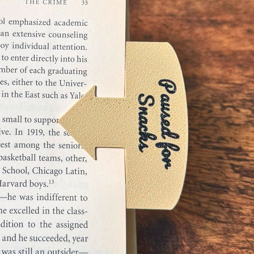 Tan bookmark spot keeper that reads Paused for Snacks in black font