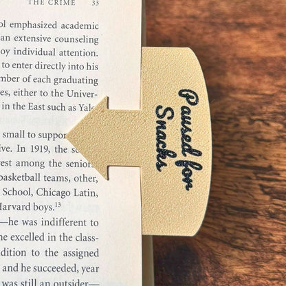 Tan bookmark spot keeper that reads Paused for Snacks in black font