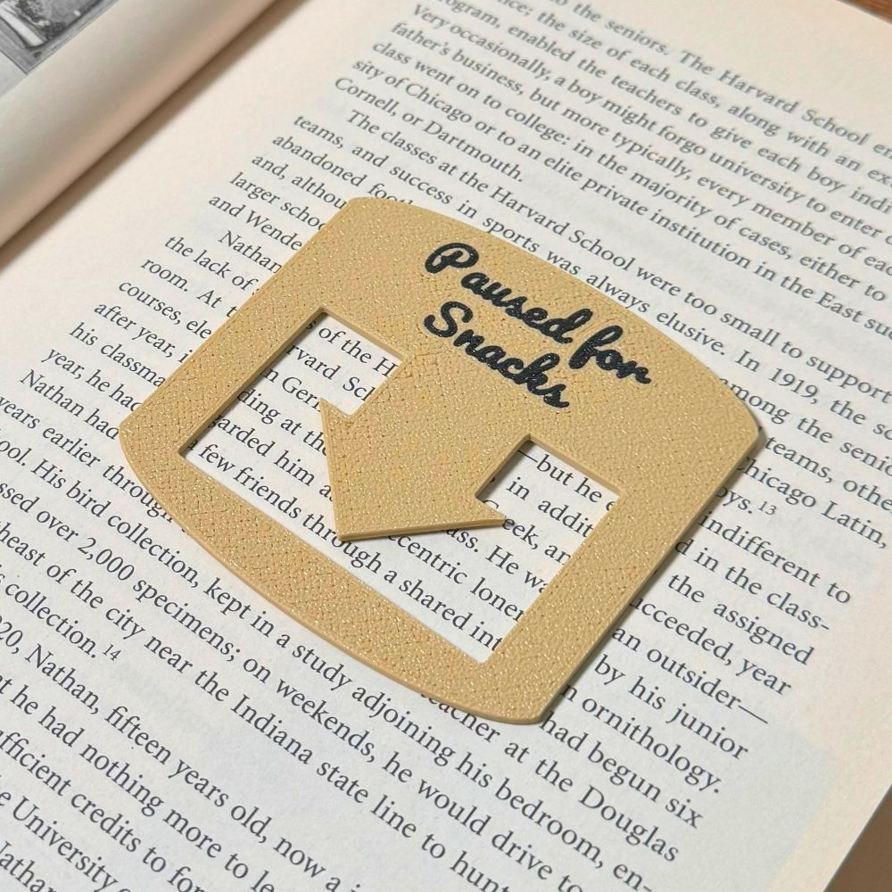 Tan bookmark spot keeper that reads Paused for Snacks in black font