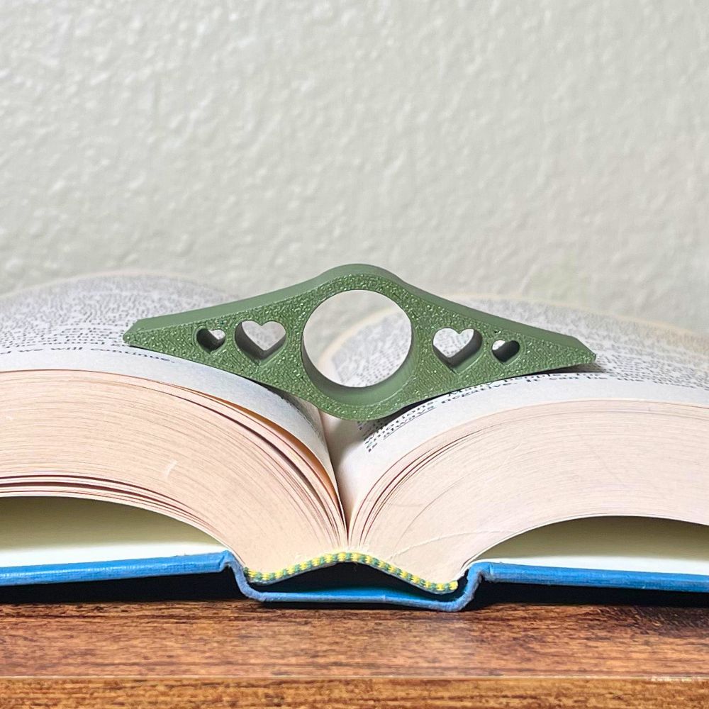 An olive book page holder with heart cut outs laying in the middle of an open book