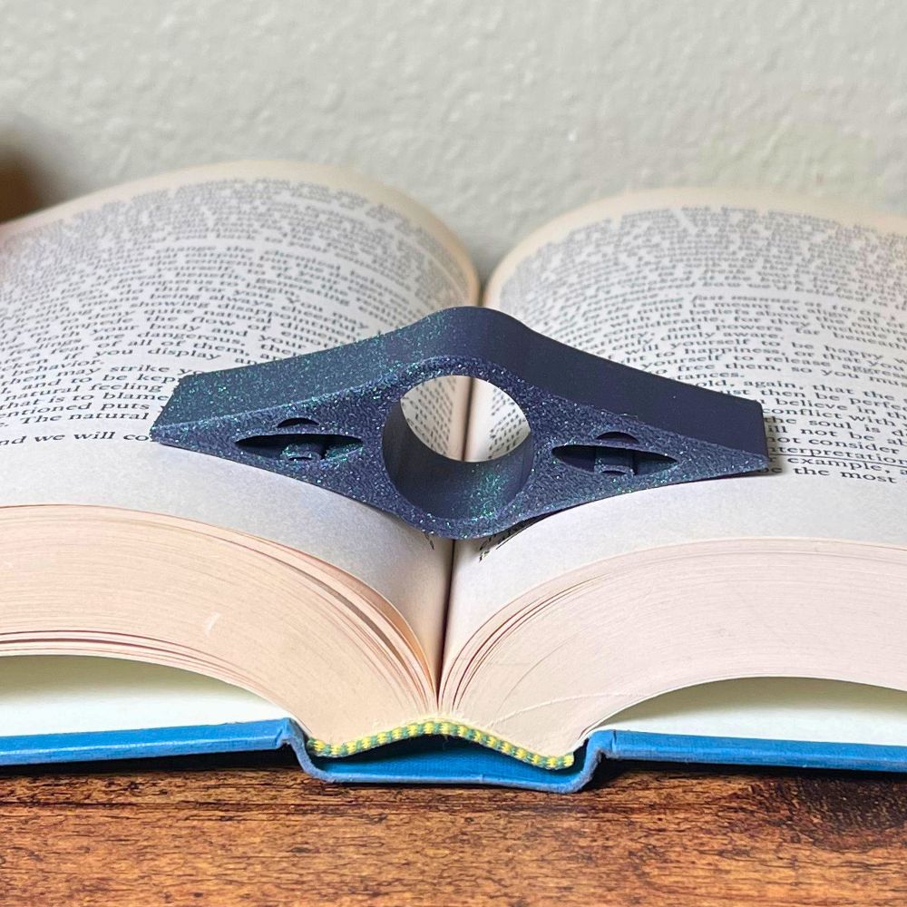An sparkly deep purple book page holder with UFO cut outs laying in the middle of an open book