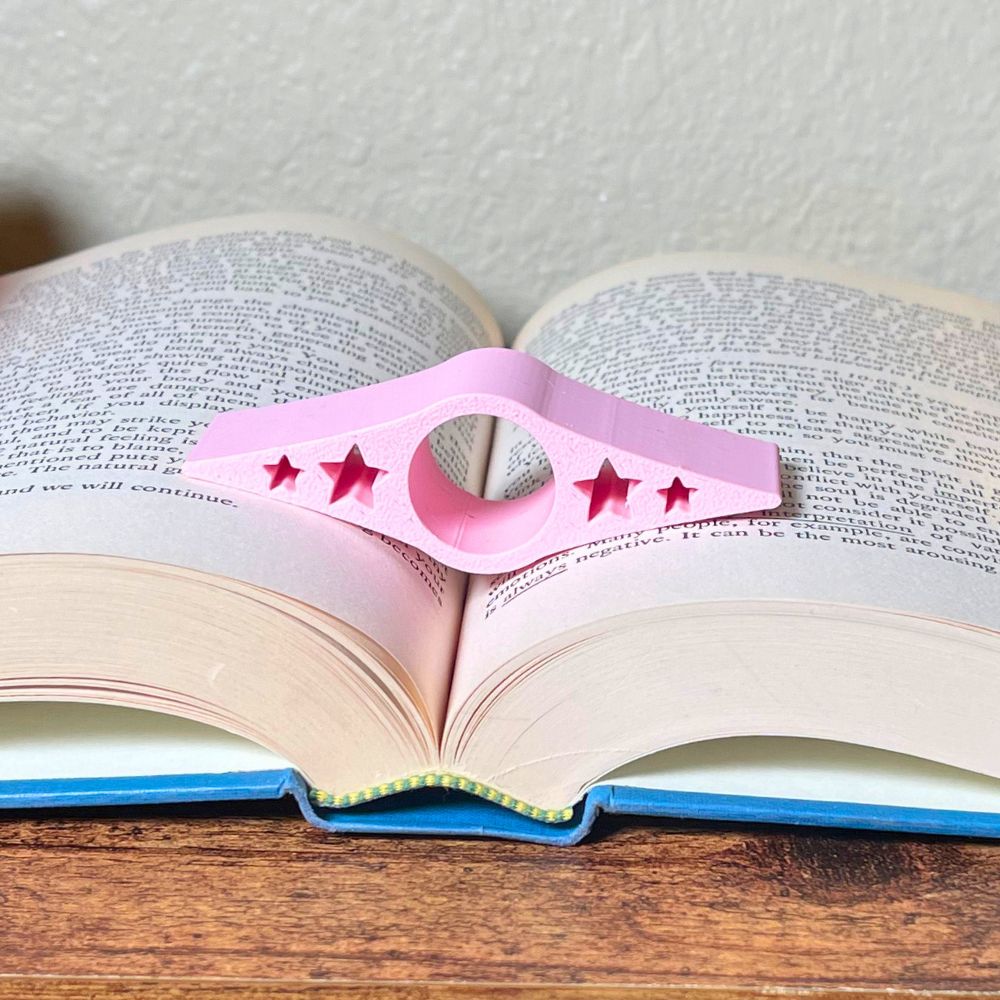A light pink book page holder with star cut outs laying in the middle of an open book