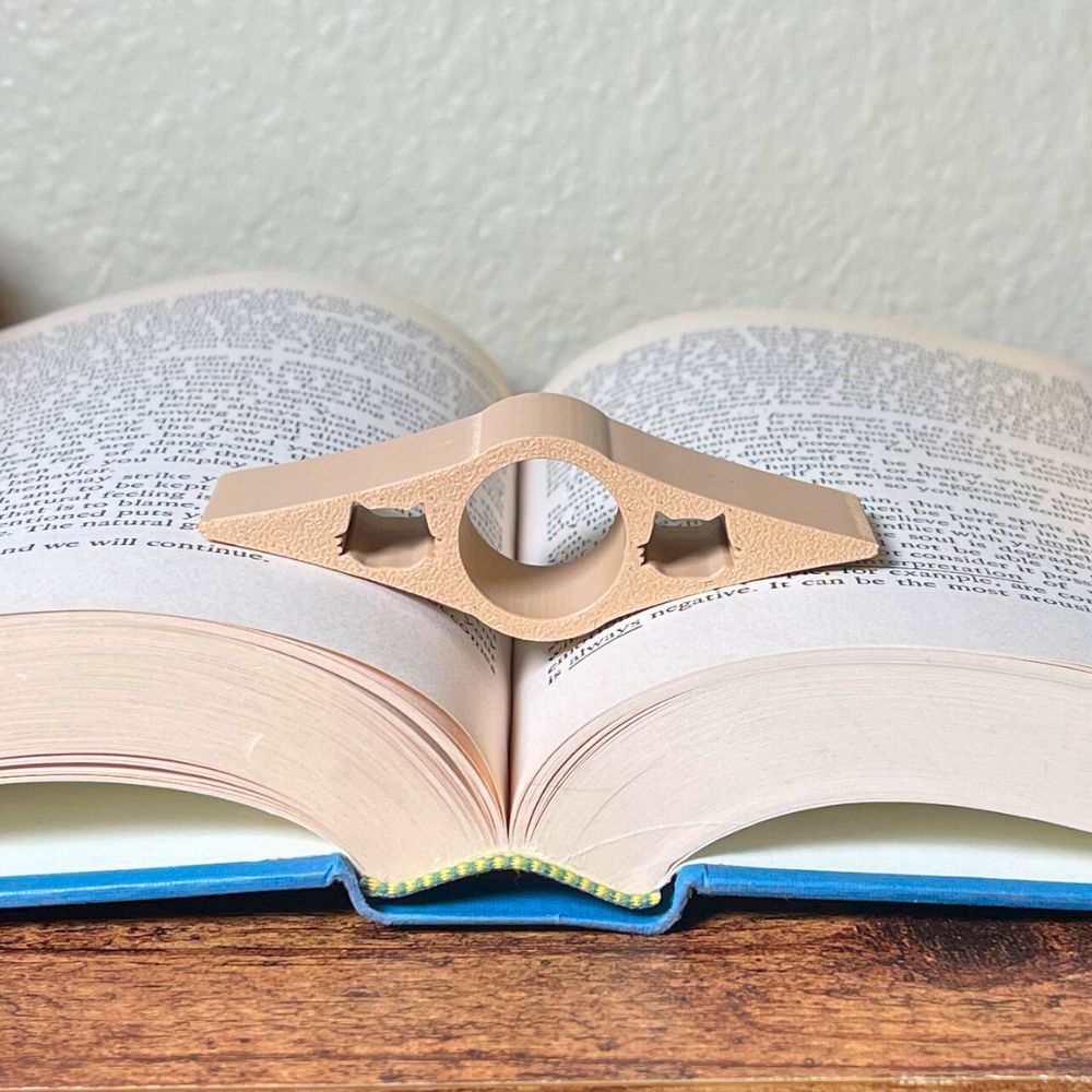 A tan book page holder with cat cut outs laying in the middle of an open book