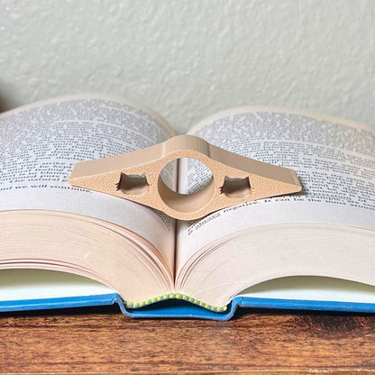 A tan book page holder with cat cut outs laying in the middle of an open book