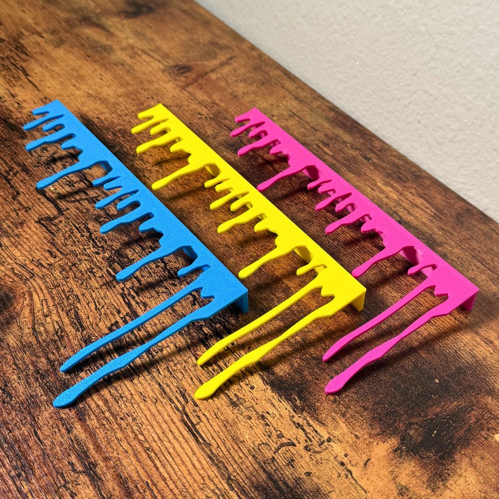 Blue Yellow and Magenta paint dripping door corner wall art laying on a wooden cabinet