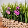 Fun flamingo plant stakes shown in a houseplant from an angle