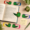 Frog bookmark clips in six colors on a desk with a book and a build your own 1, 3, or all 6 note