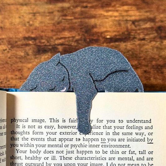 Grey cat bookmark shown in a book holding onto a page with its paw dangling