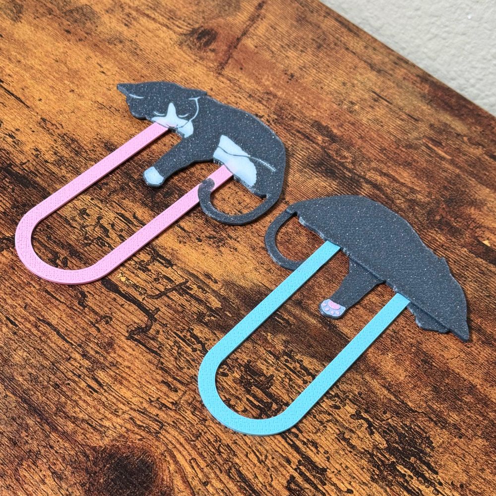 Close up angled shot of the pink and blue cat bookmarks showing the front and back of the design