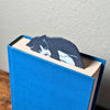 Grey tuxedo cat bookmark shown in a closed book taking a nap on top