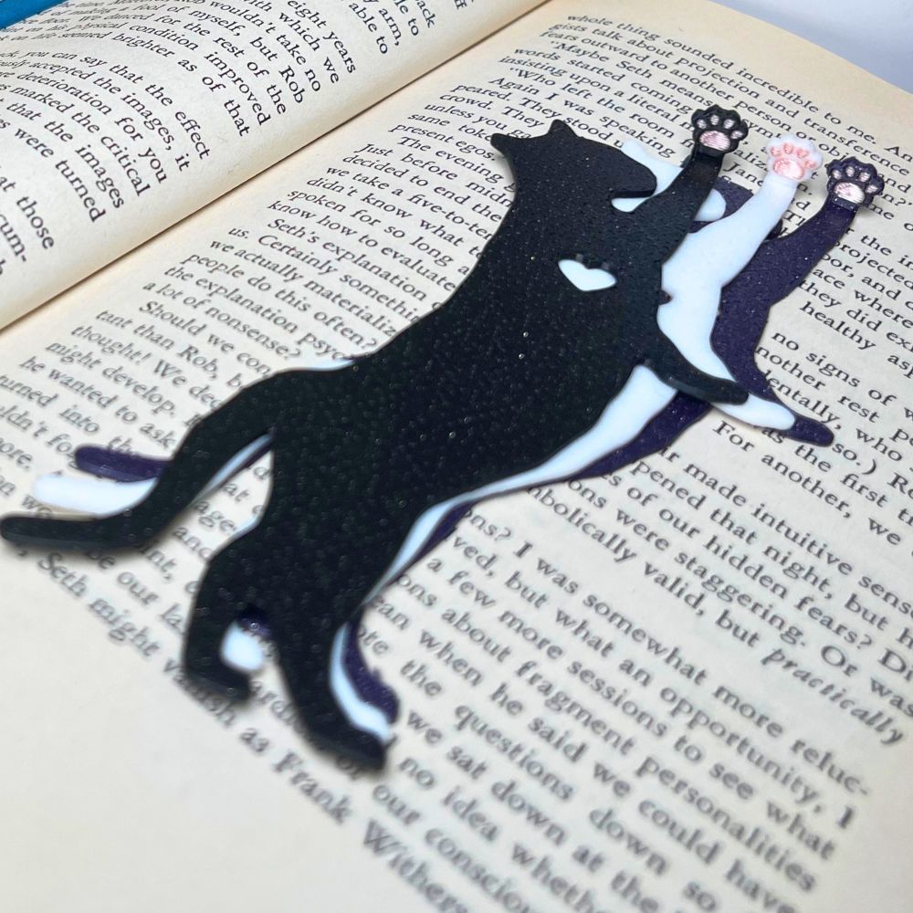 Fun cat bookmarks with a hanging paw and pink toe beans. Bookmarks shown in purple and black sparkle, as well as white