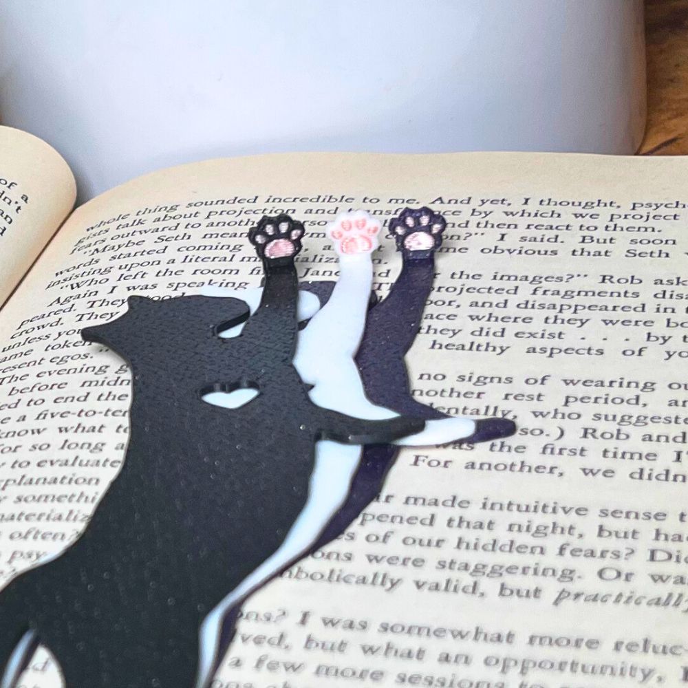 Fun cat bookmarks with a hanging paw and pink toe beans. Bookmarks shown in purple and black sparkle, as well as white