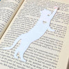 Fun cat bookmark with a hanging paw and pink toe beans. Bookmark shown in  
 white.