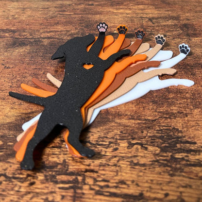 Five dog bookmarks in orange, white, tan, brown, and black sparkle laying down, showing their adorable paw toe beans on a wooden surface