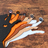 Five dog bookmarks in orange, white, tan, brown, and black sparkle laying down, showing their adorable paw toe beans close up