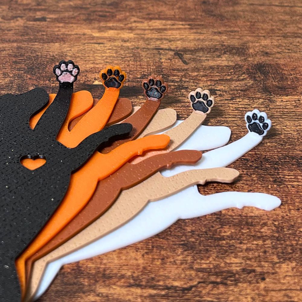 Five dog bookmarks in orange, white, tan, brown, and black sparkle laying down, showing their adorable paw toe beans close up