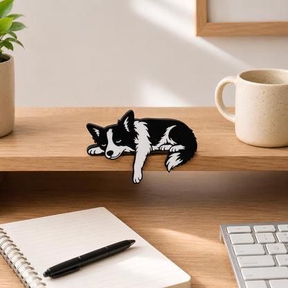 Black and white Border Collie shelf pet resting on a light wood shelf edge with a speckled mug and framed art