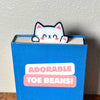 Cute kawaii style cat bookmark waving hello from a blue book showing off its cute pink toe beans