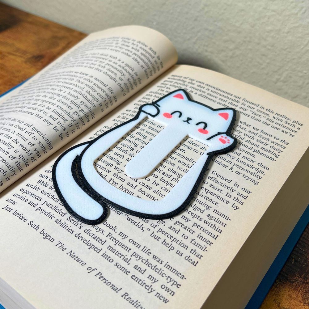 Cute kawaii style cat bookmark waving hello from inside a blue book from an angle