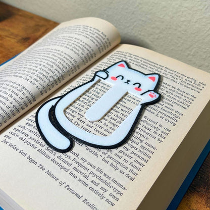 Cute kawaii style cat bookmark waving hello from inside a blue book from an angle