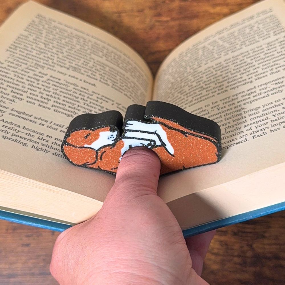 Adorable sleeping brown and white fur dog book page holder shown holding a book open from the front view