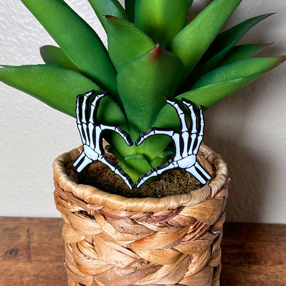 Skeleton bone hands in a heart shape inside of a houseplant