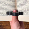 Adorable sleeping sloth book page holder shown in use holding a book open from a top view