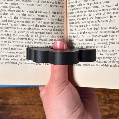Adorable sleeping sloth book page holder shown in use holding a book open from a top view