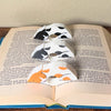 Adorable sleeping spotted cat book page holders shown in a book in orange gray and black from the front