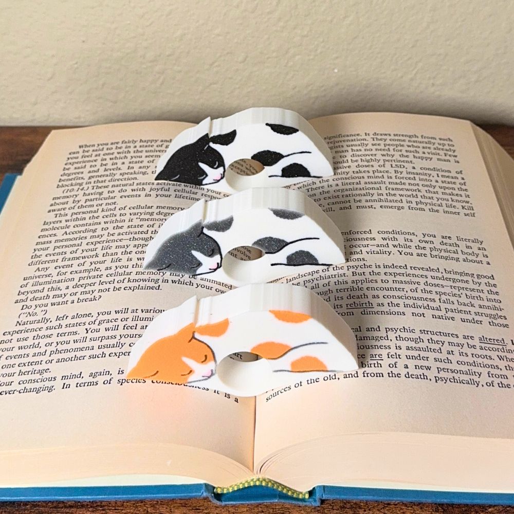 Adorable sleeping spotted cat book page holders shown in a book in orange gray and black from the front