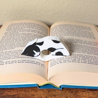 Adorable sleeping black and white spotted cat book page holder shown in a book
