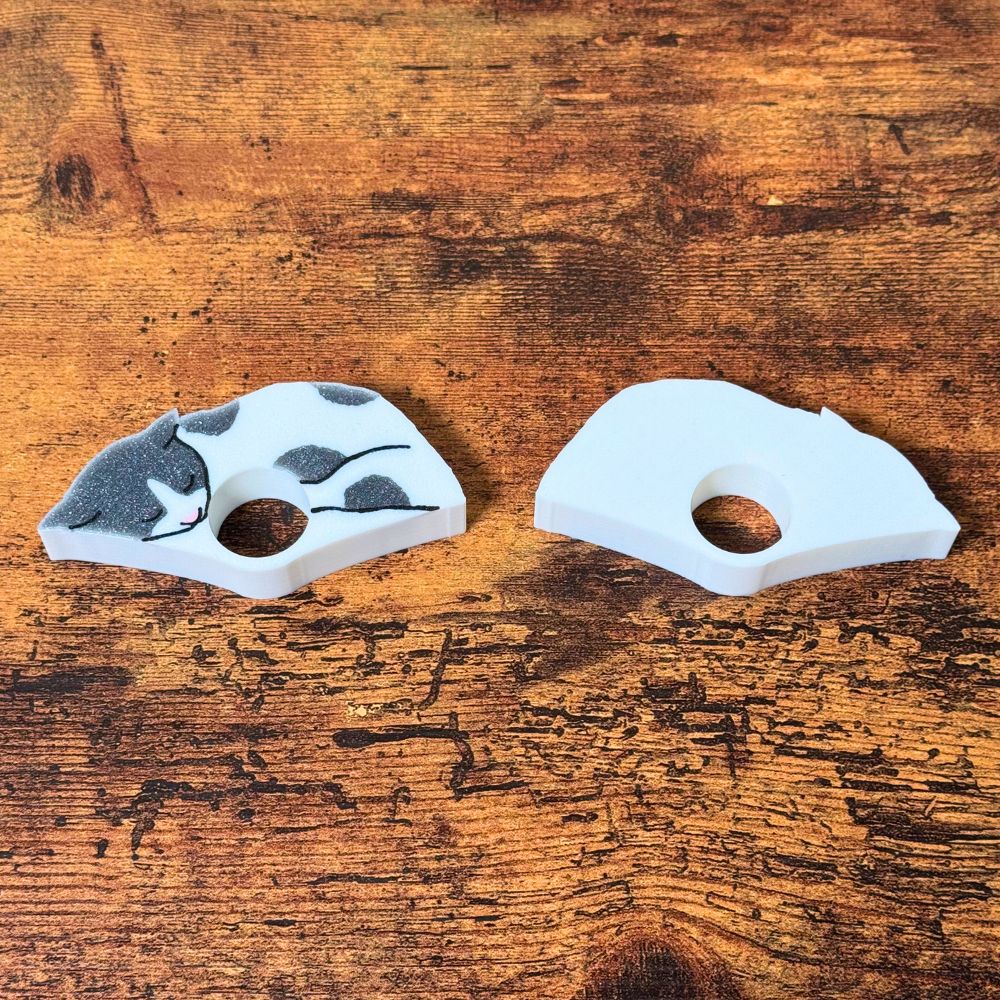 The front and back of the gray and white spotted cat page holders on a wooden table from the side view