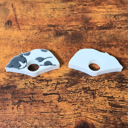 The front and back of the gray and white spotted cat page holders on a wooden table from the side view