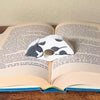 Adorable sleeping gray and white spotted cat book page holder shown in a book