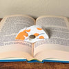 Adorable sleeping orange and white spotted cat book page holder shown in a book