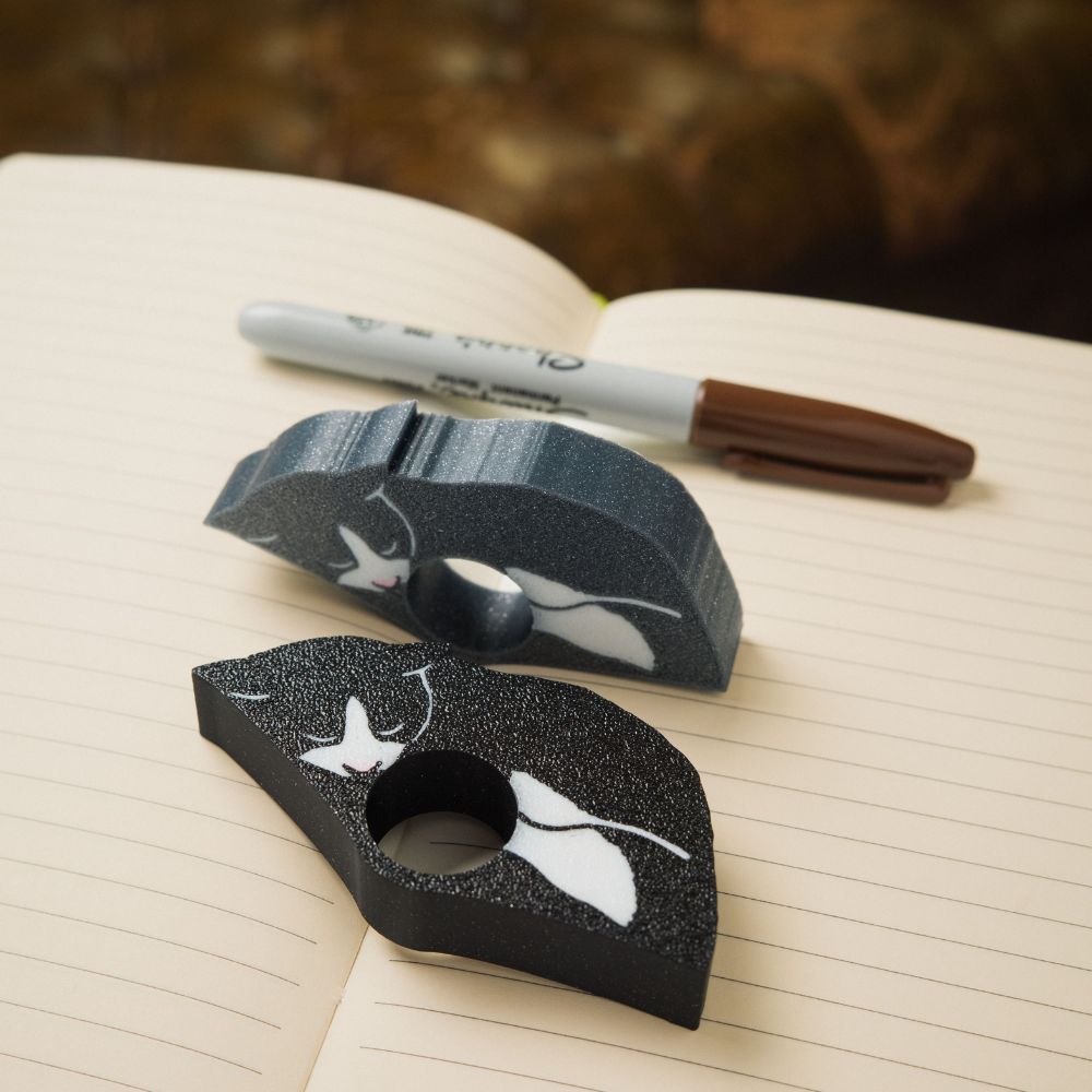Sleepy black and grey tuxedo cat page holders resting in a planner next to a brown permanent marker
